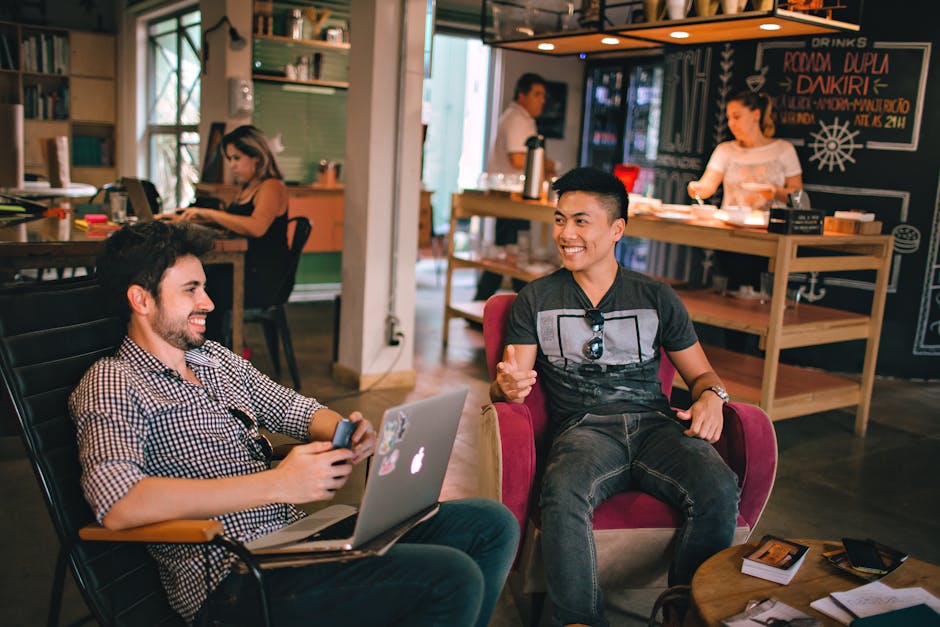 Dois homens desfrutando de uma conversa descontraída com laptops em um café coworking aconchegante no Brasil.